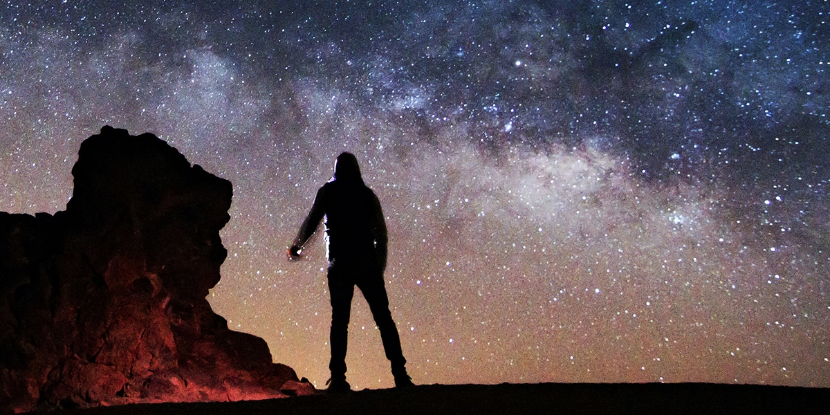 man standing in the desert looking up at the universe