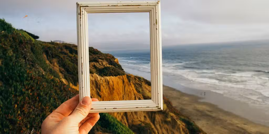 Hand holding a picture frame, framing in nature in the background.