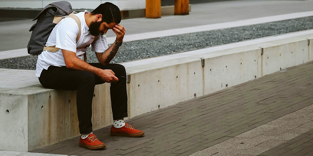 man being sad, resting his head in his hand, sitting outside