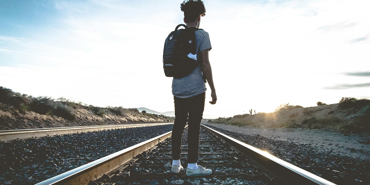 young person walking on train tracks during sunrise