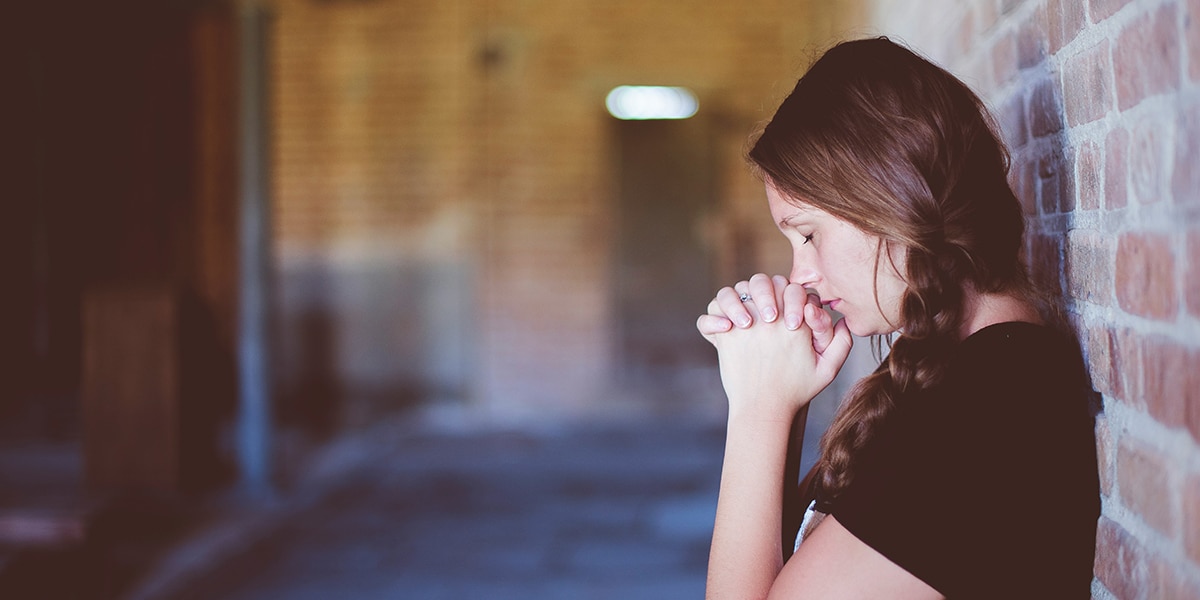 teenager with folded hands leaning against a wall praying