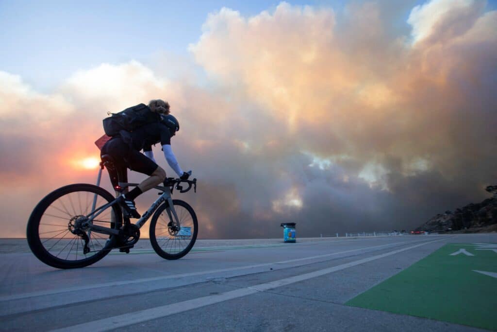 A man rides a bike with his dog in a backpack as the Palisades fire burns during a weather-driven windstorm on the west side of Los Angeles Jan. 7, 2025. (OSV News photo/Ringo Chiu, Reuters)