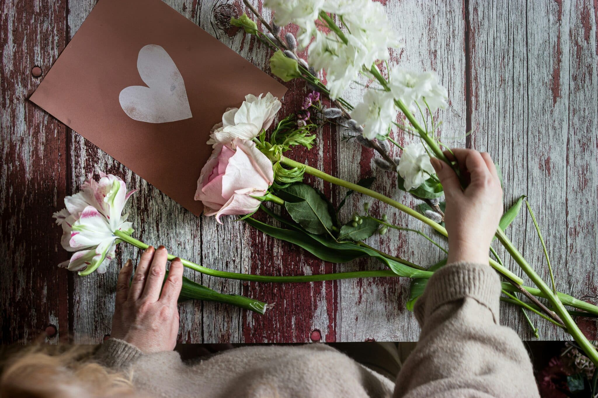 Woman arranging flowers on a wooden table |n Photo by micheile henderson on Unsplash