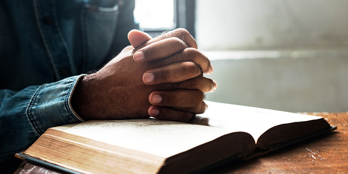 Folded hands in prayer over a open Bible
