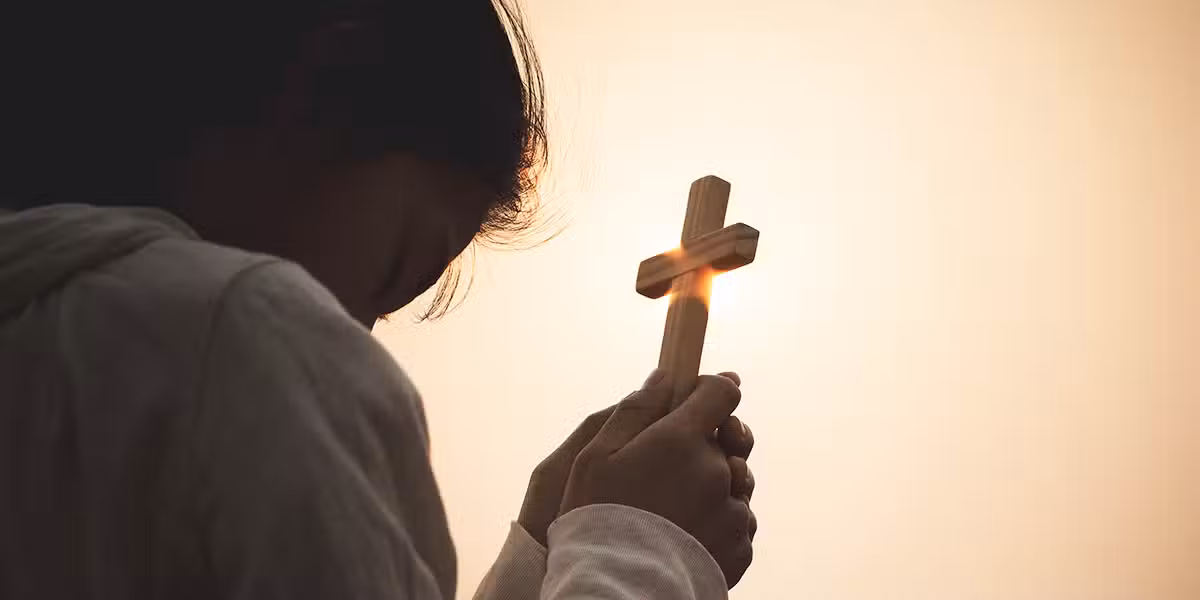 woman holding a cross and praying early in the morning during sunrise