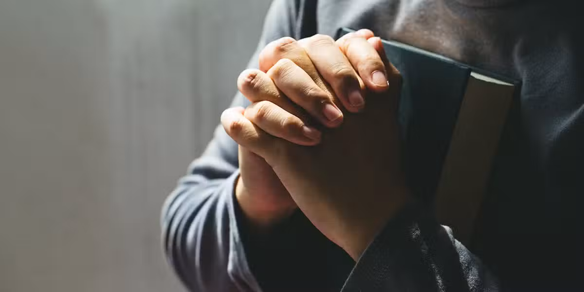 folded hand in prayer while holding a Bible