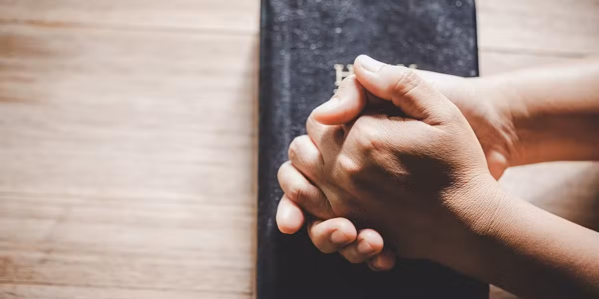 hands folded over a Bible in prayer