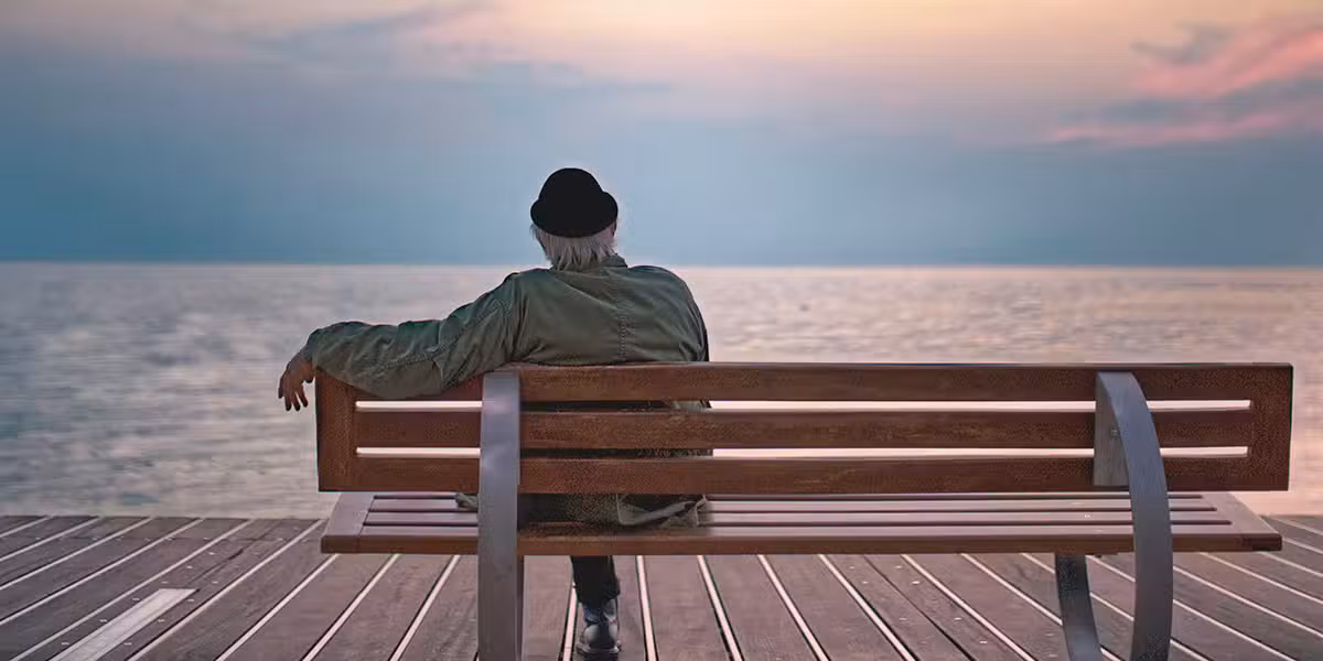 older man sitting peacefully on a bench overlooking an ocean