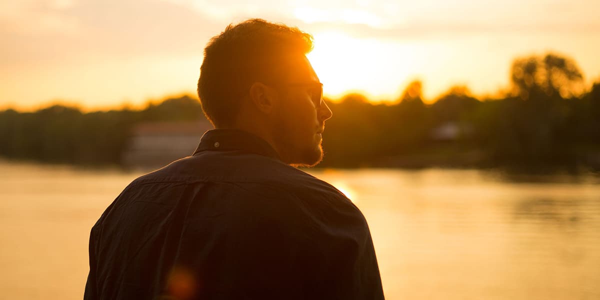 man standing silently in front of a sunset