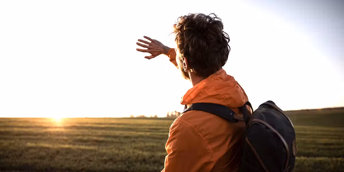 man is holding his hand in front of his face because of the blinding sun.