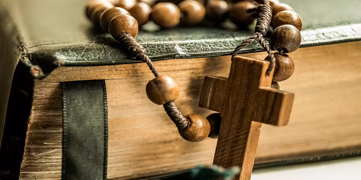 bible and a rosary with a wooden cross attached.