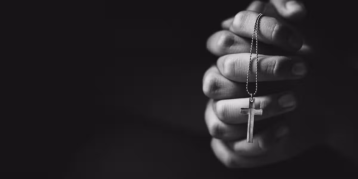 person praying with folded hands while holding a rosary