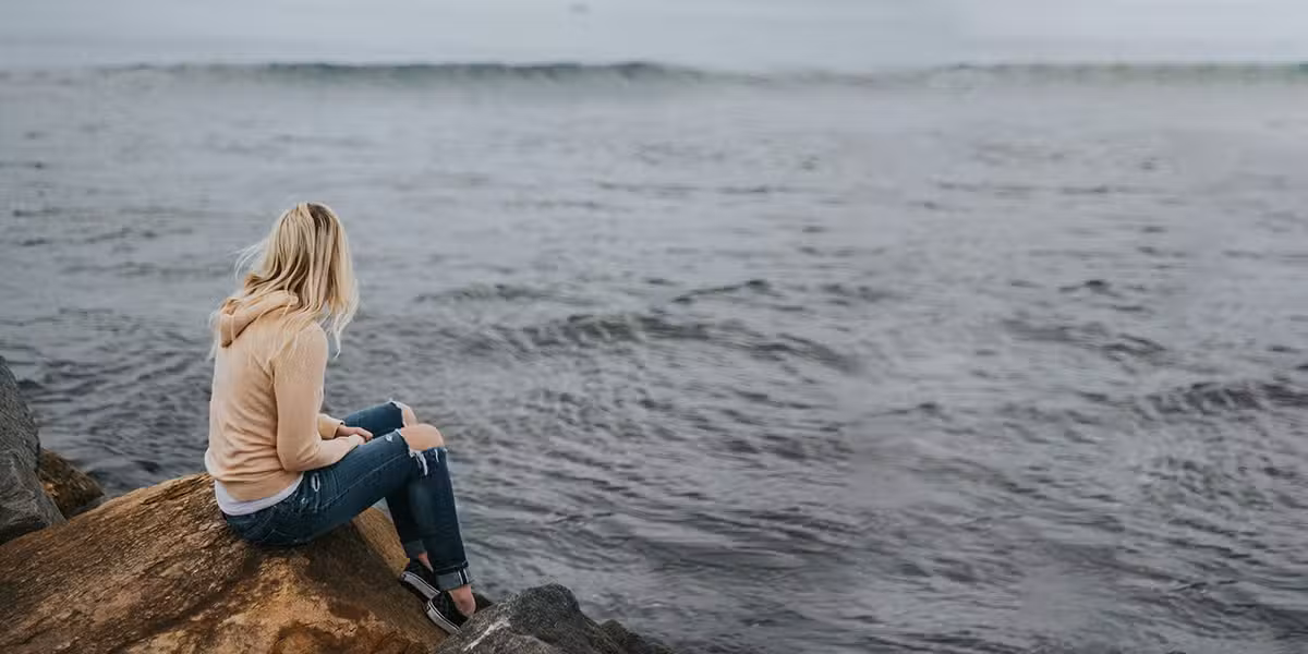 woman sitting on rocks by the ocean with waves in the distance.