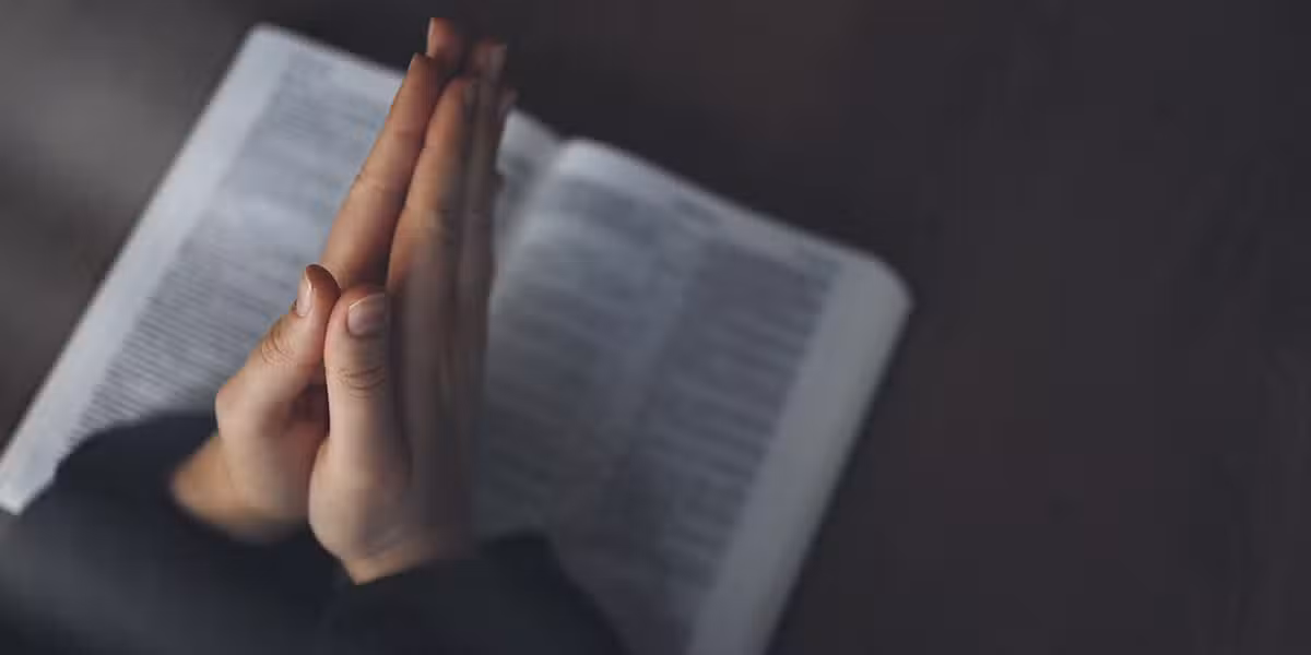 hands folded in prayer above a Bible