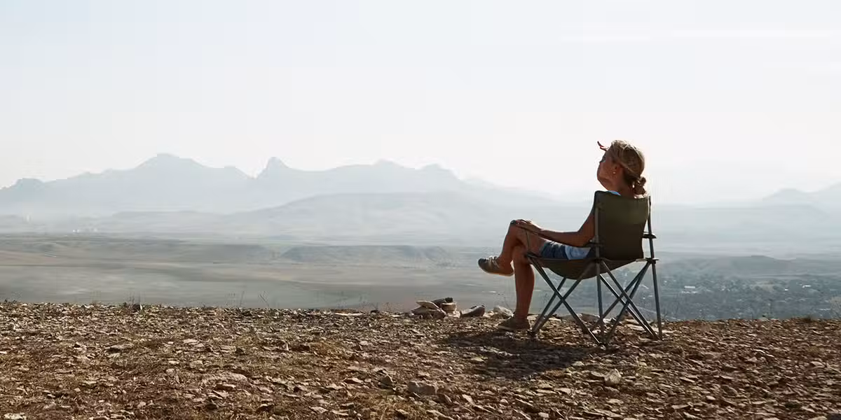 woman sitting in a chair outside with mountains in the background.