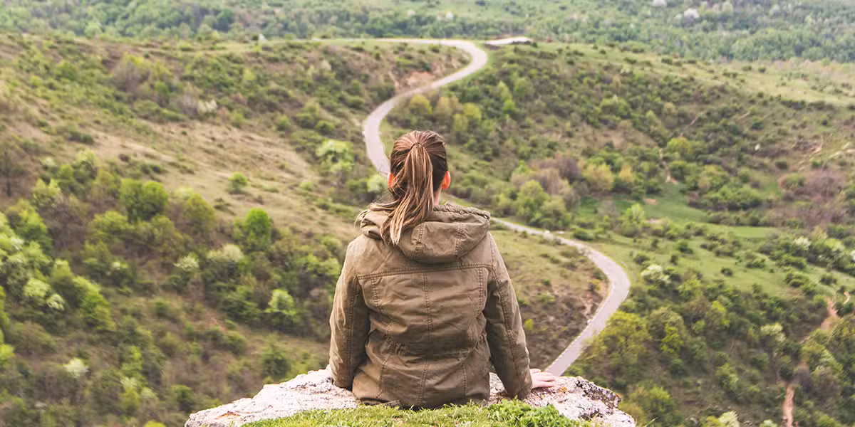 woman sitting on a rock overlooking a valley during her journey