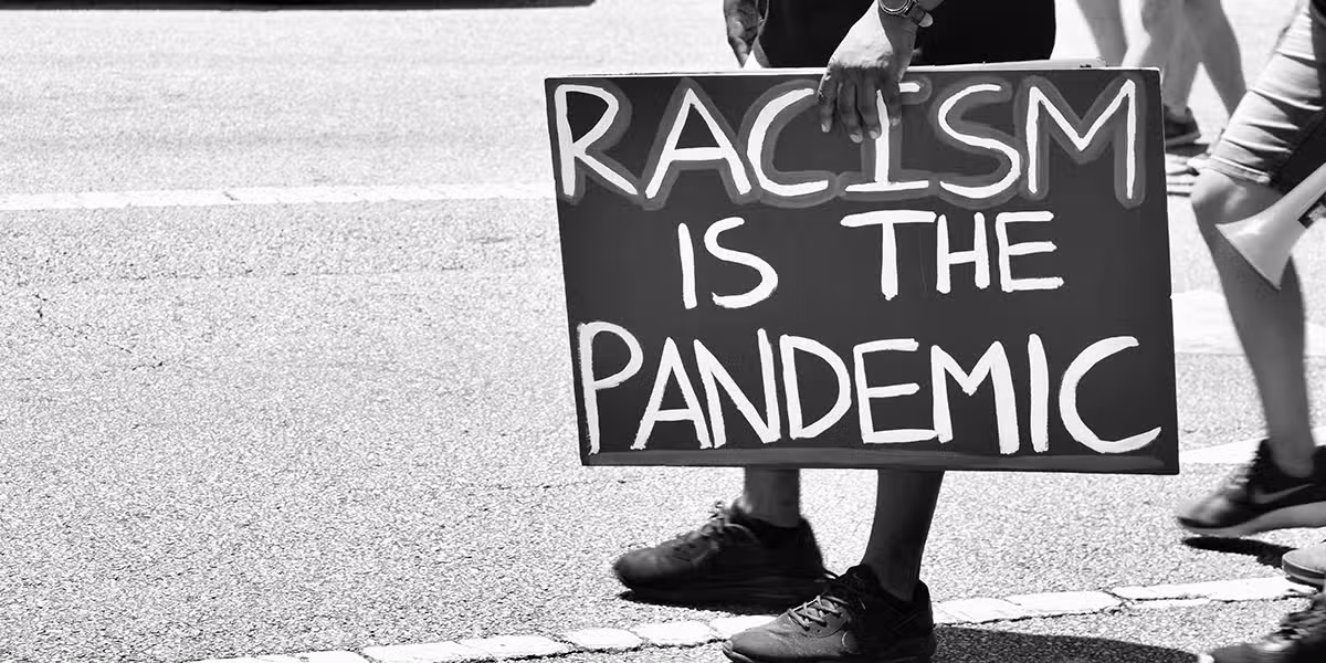 person holding cardboard sign with the words "Racism is the Pandemic"