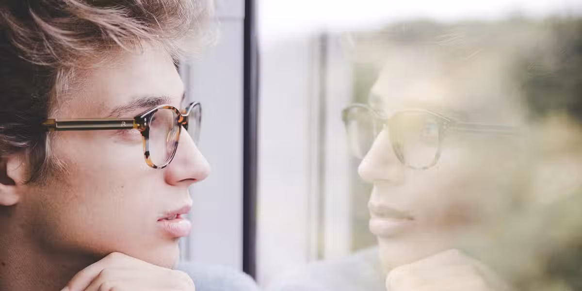 young man looking through a window that mirrors his face like a photocopy.