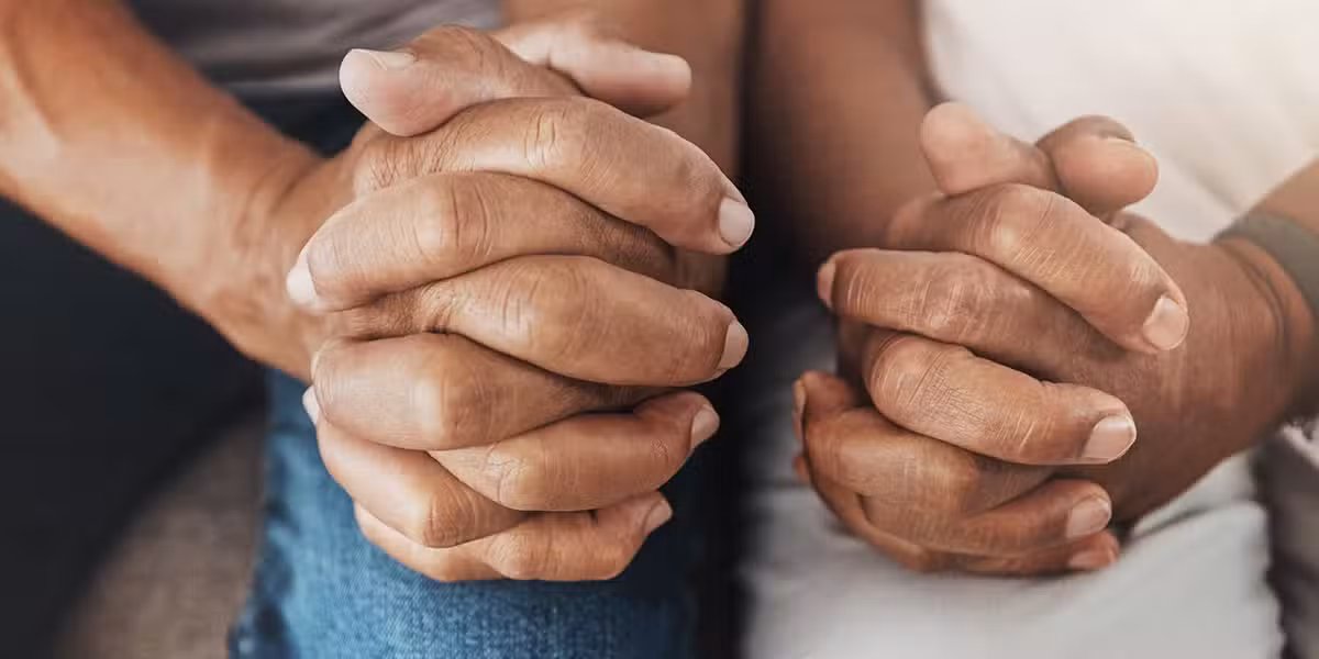 Two people praying together with folded hands.