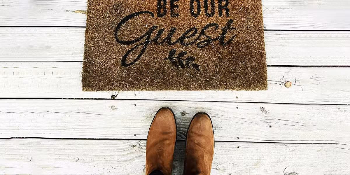 shoes standing in front of a welcome mat with the words "Be Our Guest"