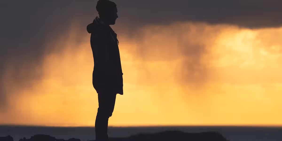 silhouette of a man with dark stormy clouds and sunset in the background