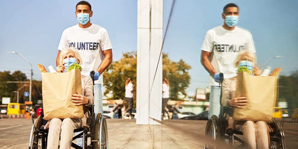 A volunteer is helping a senior in a wheelchair, bringing home grocery.