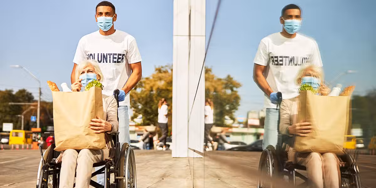 A volunteer is helping a senior in a wheelchair, bringing home grocery.