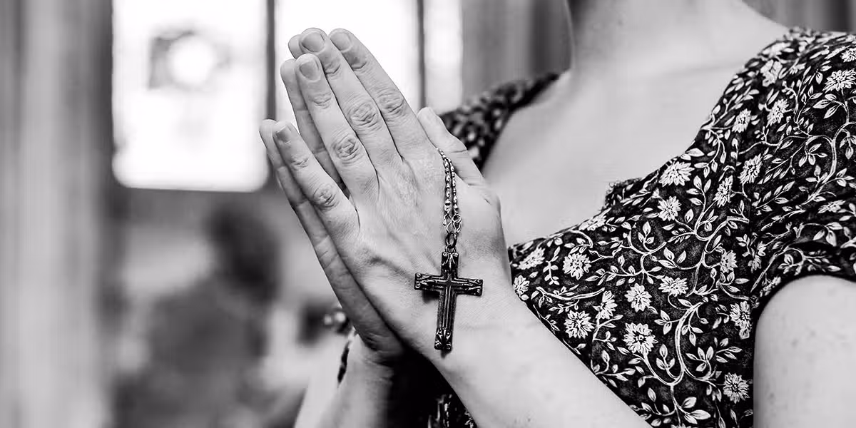 woman praying with folded hands while holding a rosary.