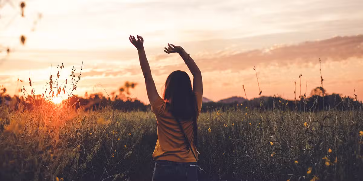 woman rejoicing in a field while watching a sunrise.
