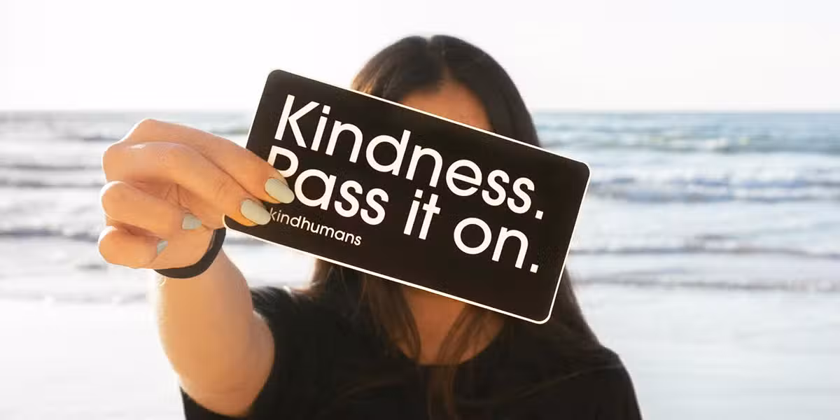 woman holding a sign with the words "Kindness Pass It On" printed on it.