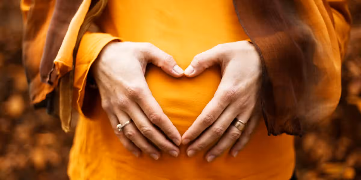 woman holding her hands forming a heart over her pregnant belly
