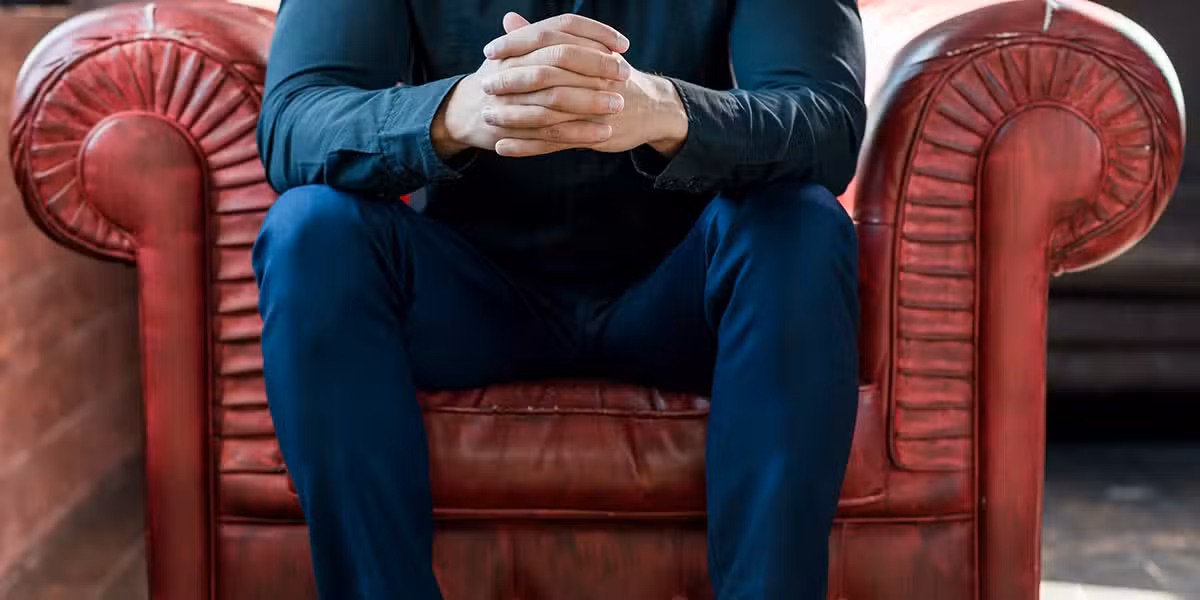 man sitting in a big red arm chair with his hands folded.