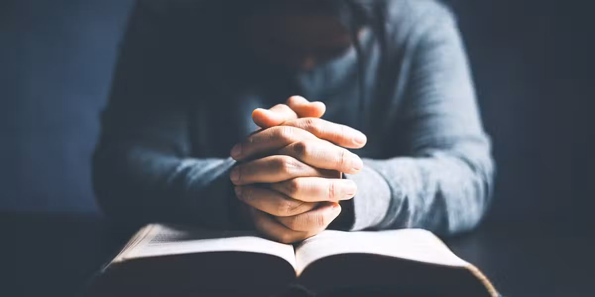 person praying with folded hands over their Bible.