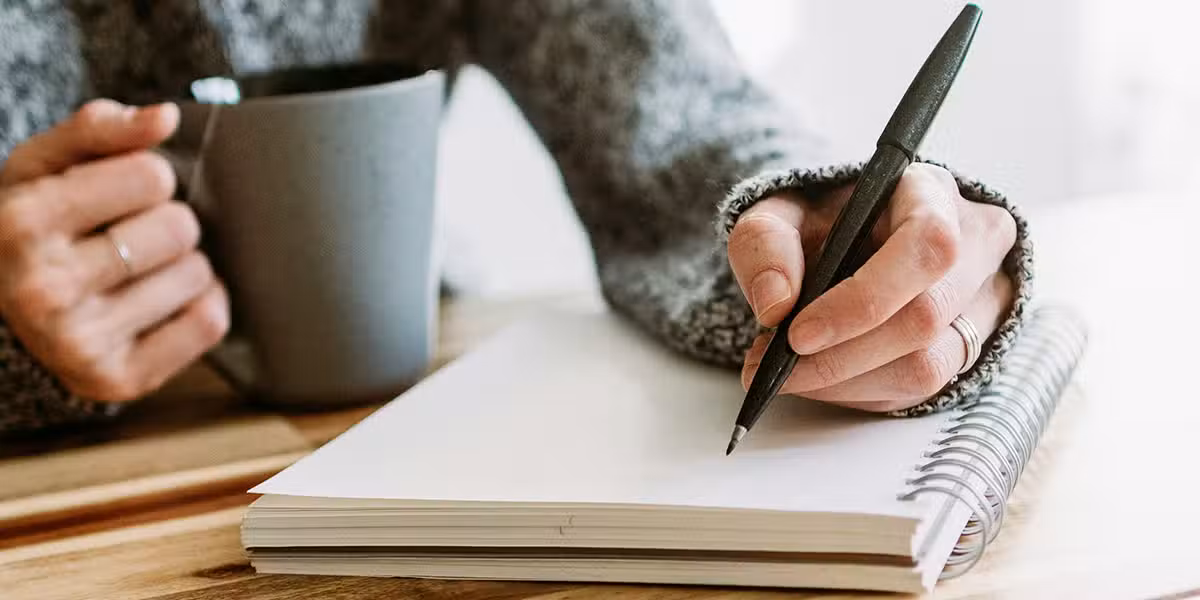 hand writing into a notebook with a pen