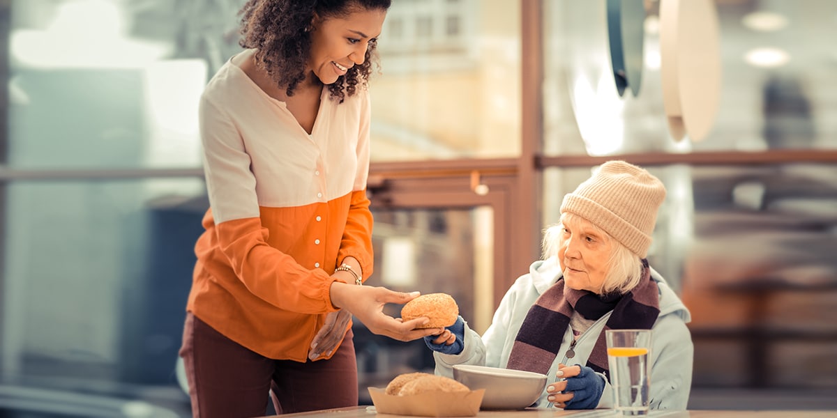woman helping homeless woman with food,