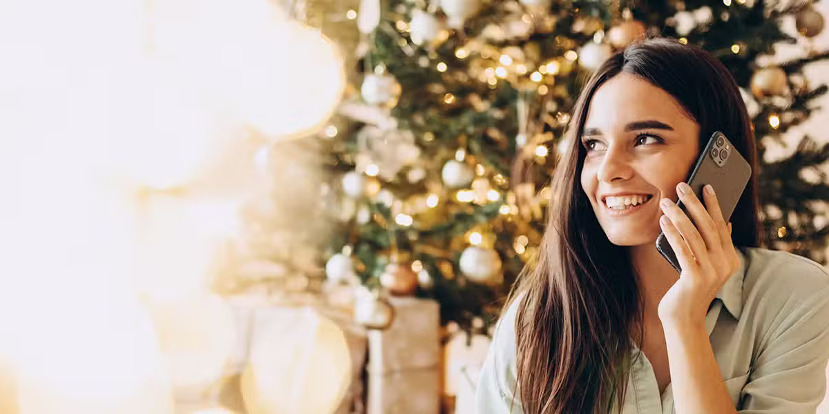 the celebration of christmas; woman on her cellphone in front of a Christmas tree.