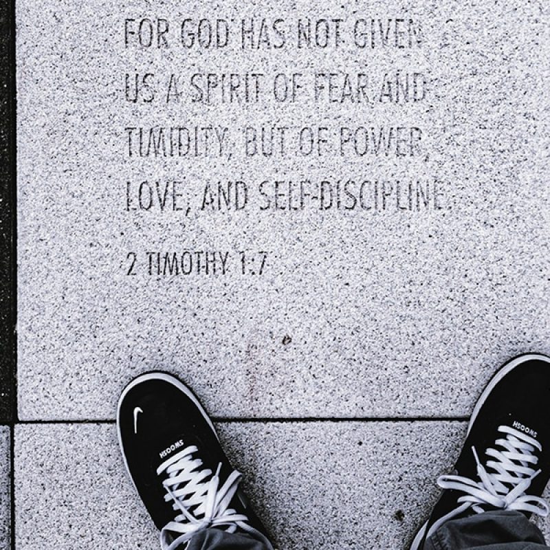 black sneakers standing next to a bible verse engraved in stone tile.