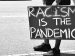 person holding cardboard sign with the words "Racism is the Pandemic"