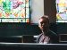 Man sitting in church with stainless windows behind him.