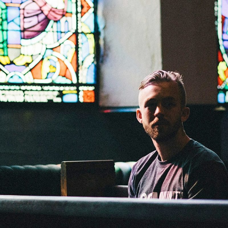 Man sitting in church with stainless windows behind him.
