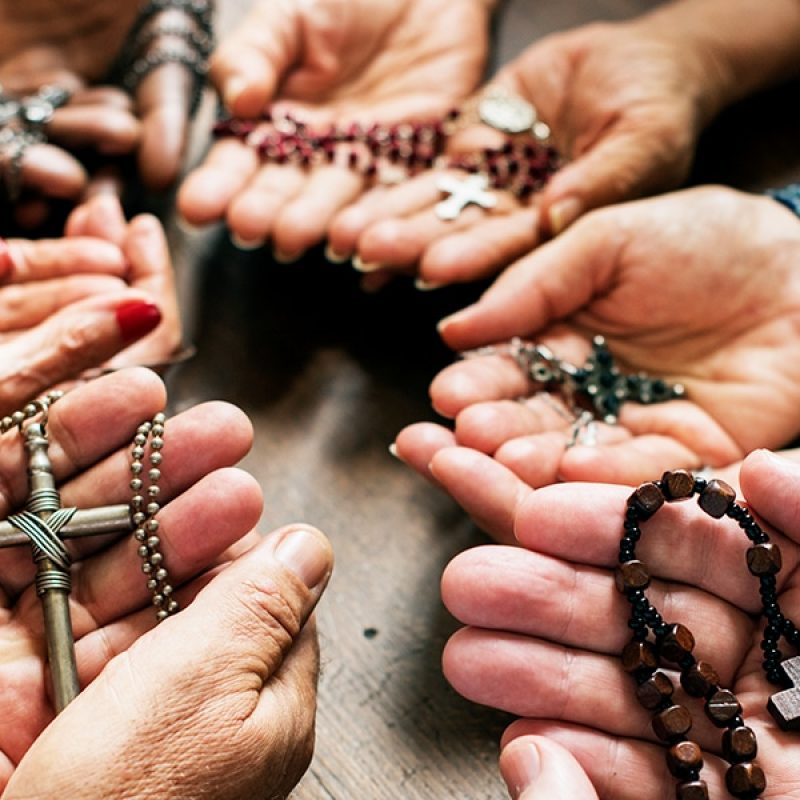 group of people in a circle holding rosaries and praying