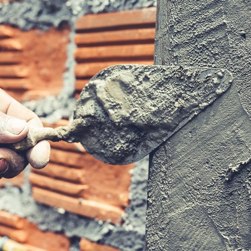 hand using a trowel to put cement on a brick wall
