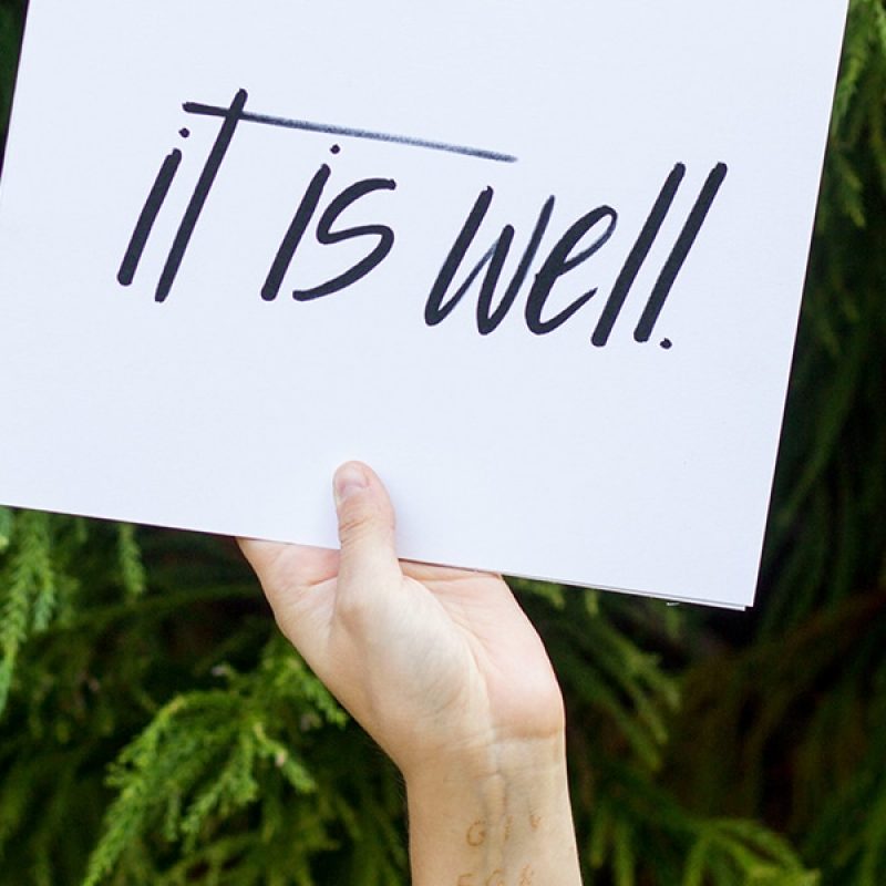 hand is holding a sign with the words "It Is well"