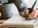 hand writing into a notebook with a pen