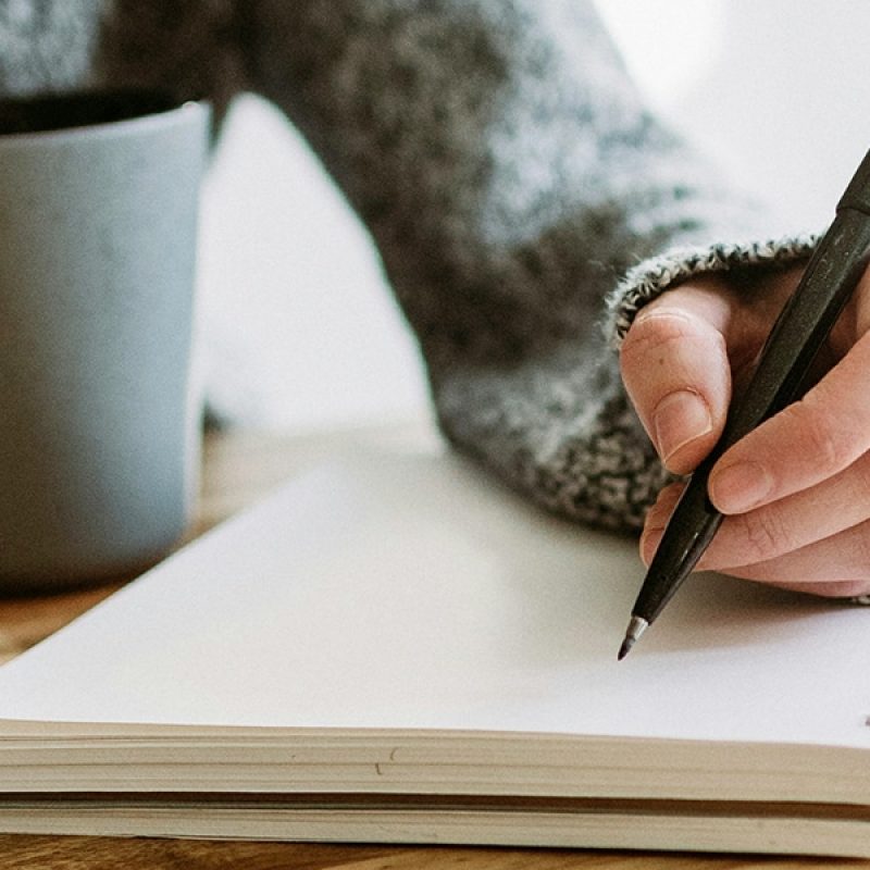 hand writing into a notebook with a pen