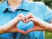 two hands are forming a heart in front of the person's chest.