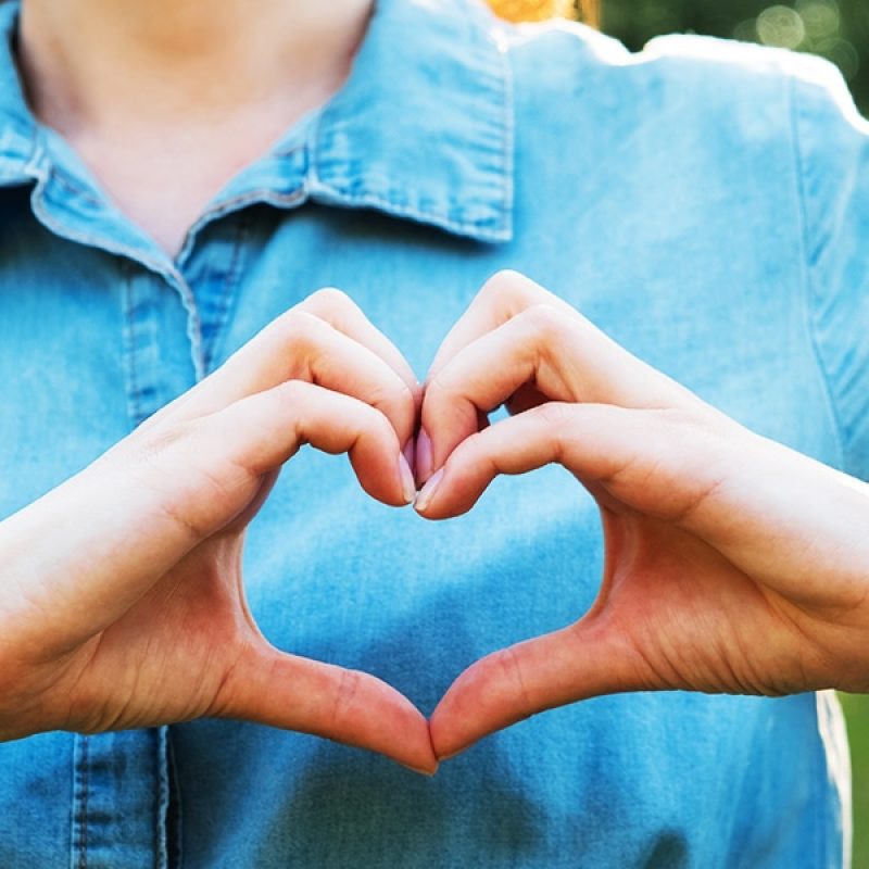 two hands are forming a heart in front of the person's chest.