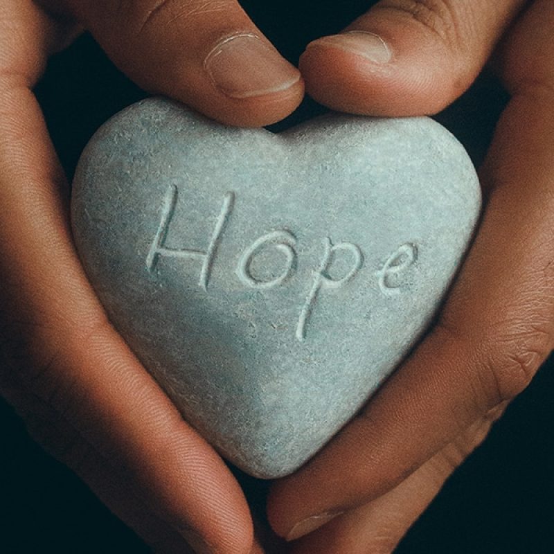 hands holding a stone heart with the word hope carved in it