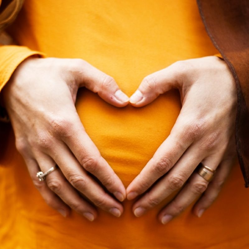 woman holding her hands forming a heart over her pregnant belly