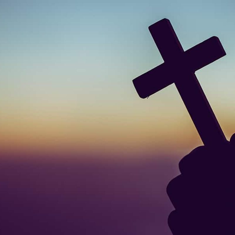 hands holding a cross with a sunset in the background